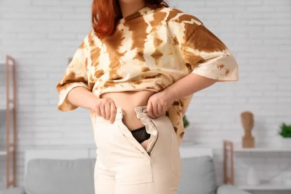Image of woman trying to do her trousers up after pregnancy weight gain Kingston upon Thames