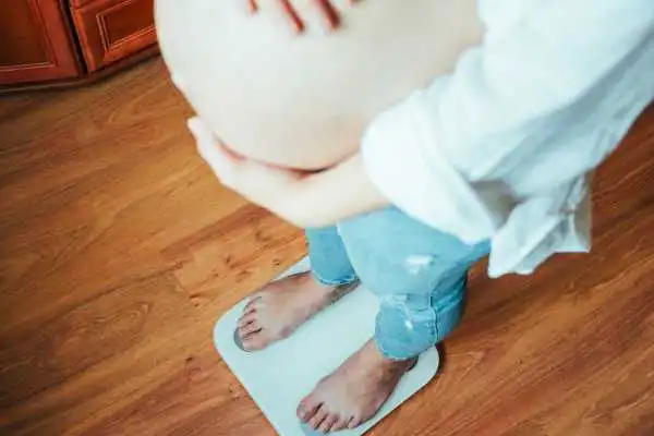 Image of woman weighing herself and experiencing weight gain through pregnancy Kingston upon Thames
